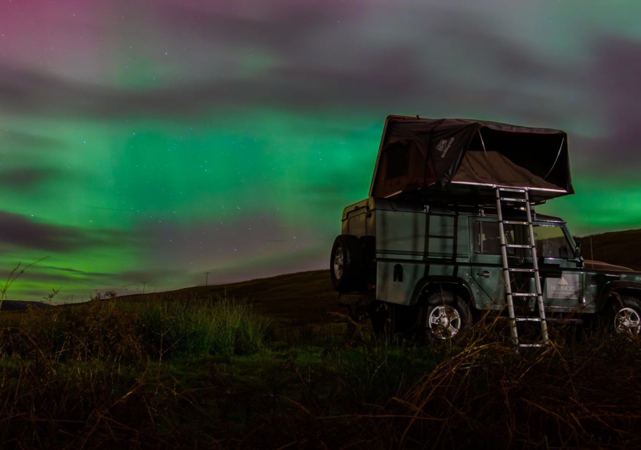 A Nomadic Scotland Land Rover with the Northern lights behind it in Scotland