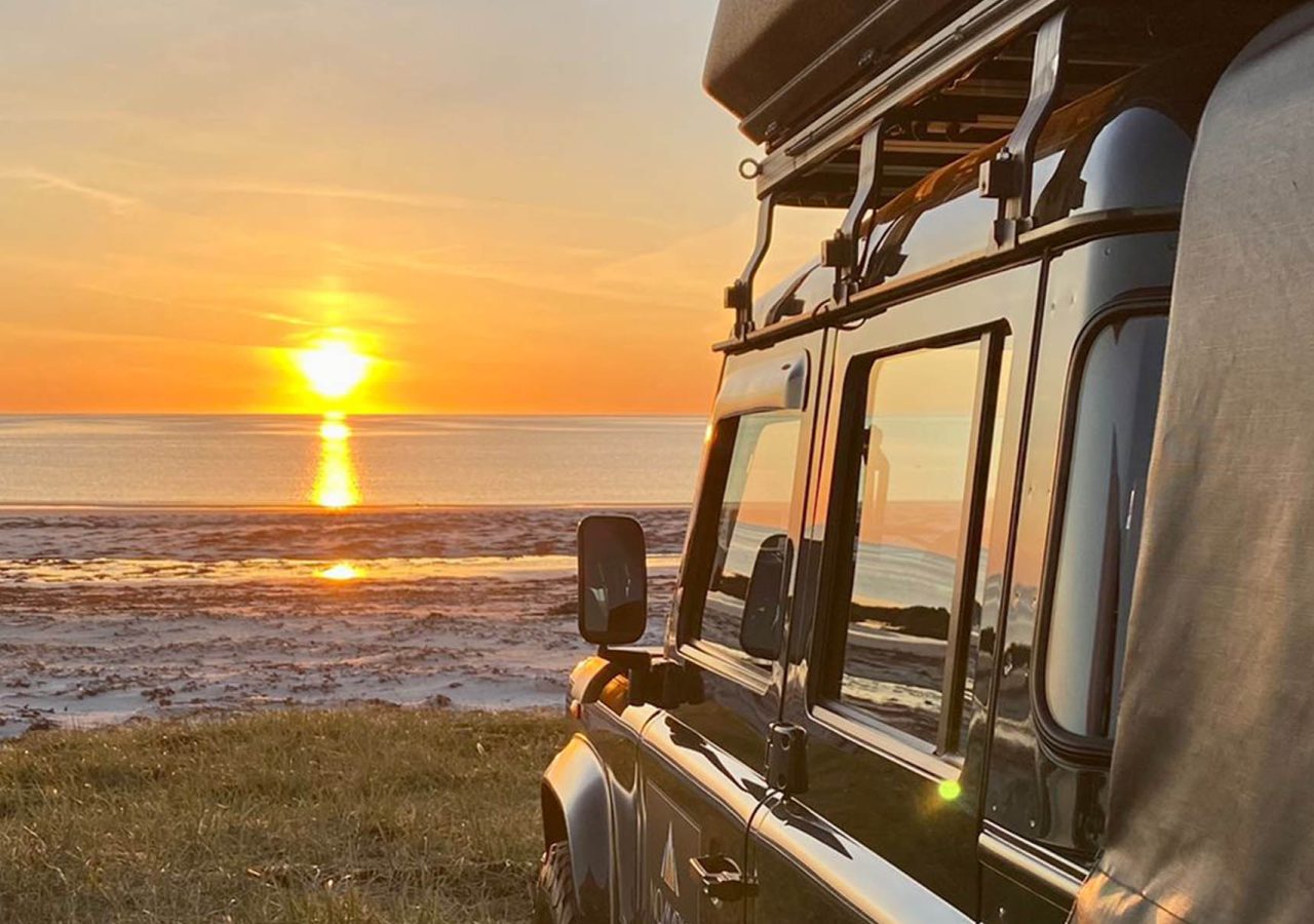 A Nomadic Scotland Land Rover overlooking a beach with a sunset in Scotland