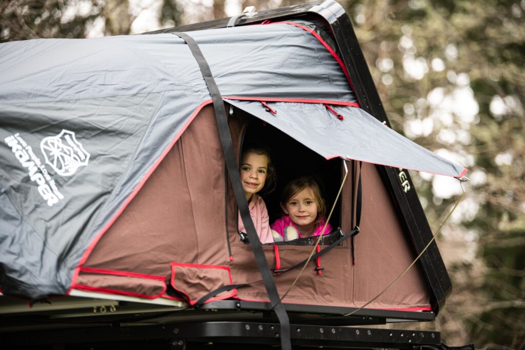 Two kids peeking out of a Nomadic Scotland Roof top tent