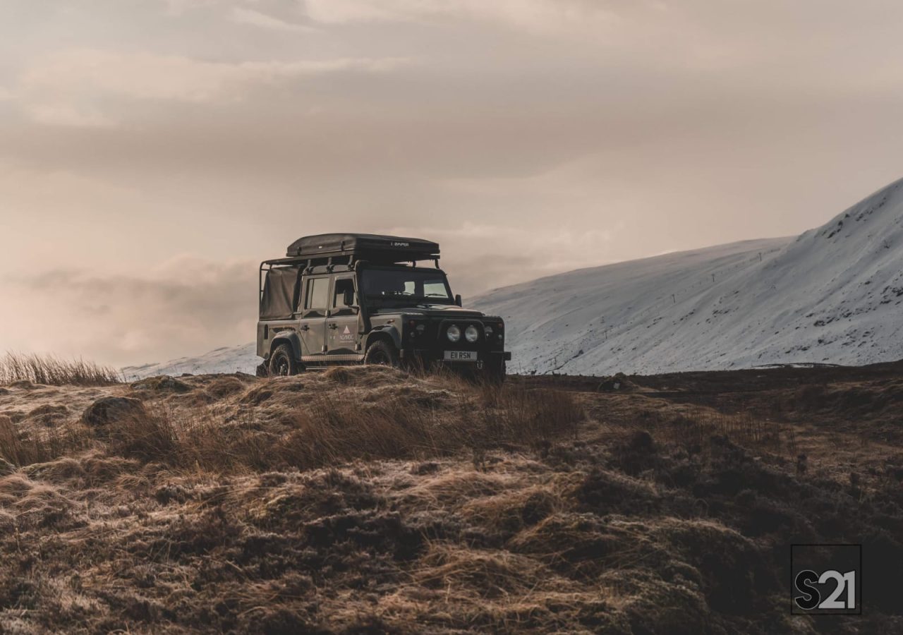 Car perched on hill overlooking Scottish mountains.