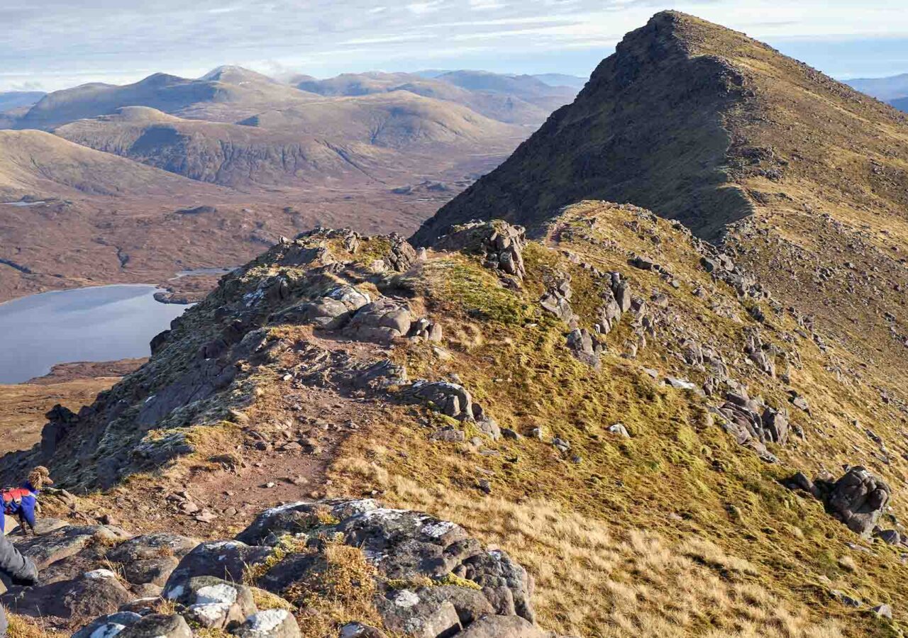 A hiker sitting looking at a ridge to the top of a munro