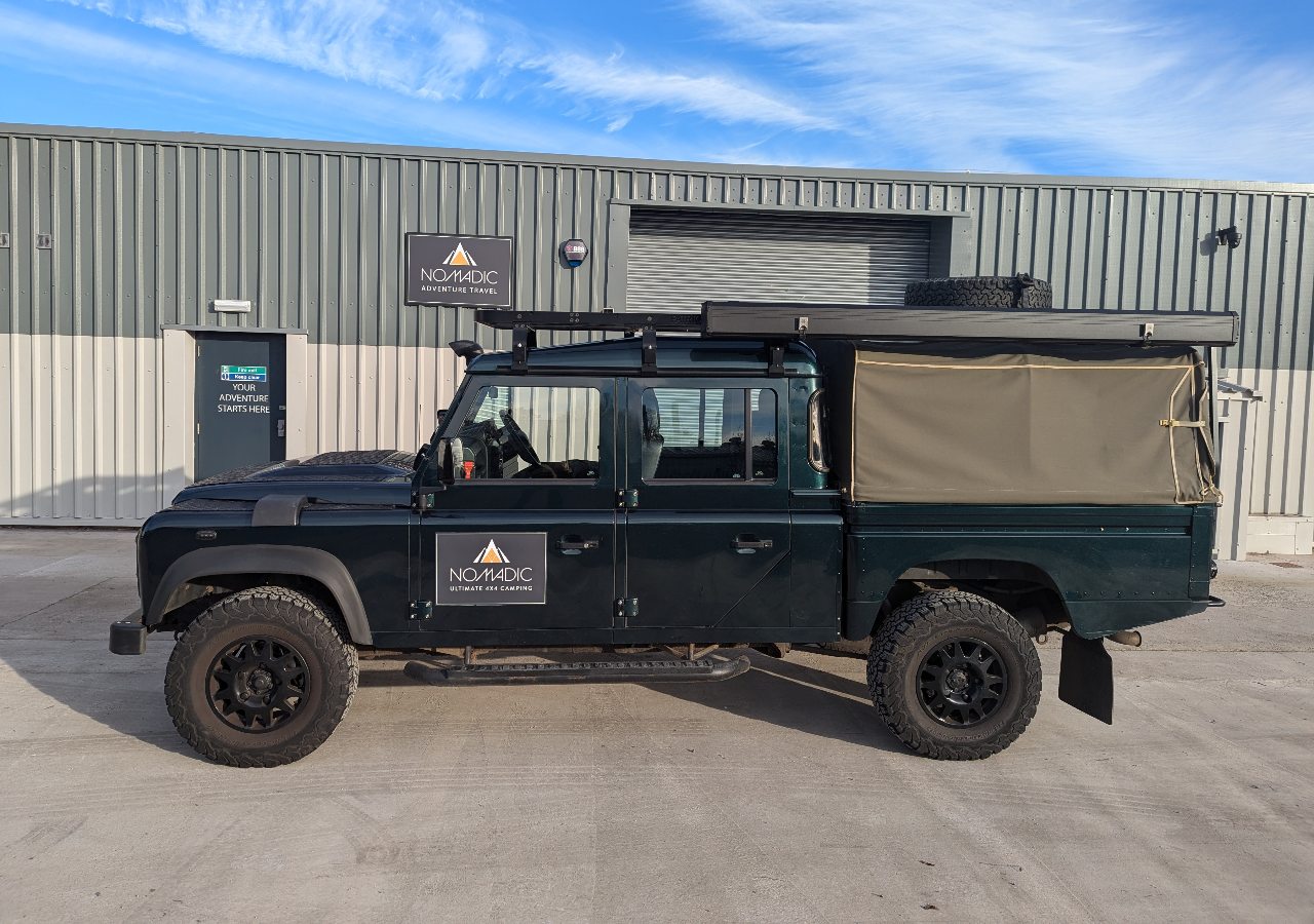 A Land Rover Defender 130 4x4 vehicle for hire on a sunny day in Scotland.