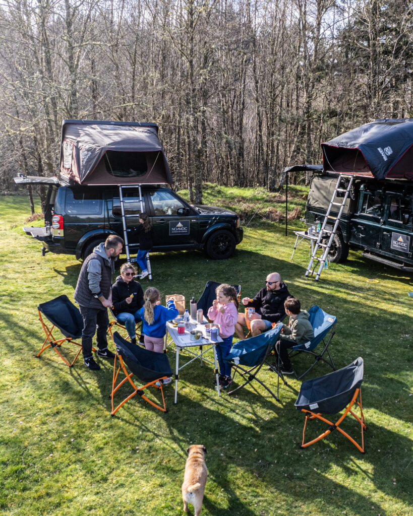 Family enjoying a camping trip with two Nomadic Scotland cars parked in the background