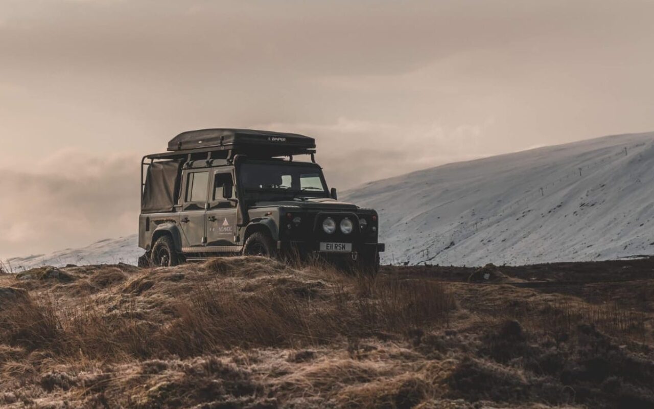 A Landrover Defender in the rugged Scottish Highlands in Winter with a snowy backdrop.