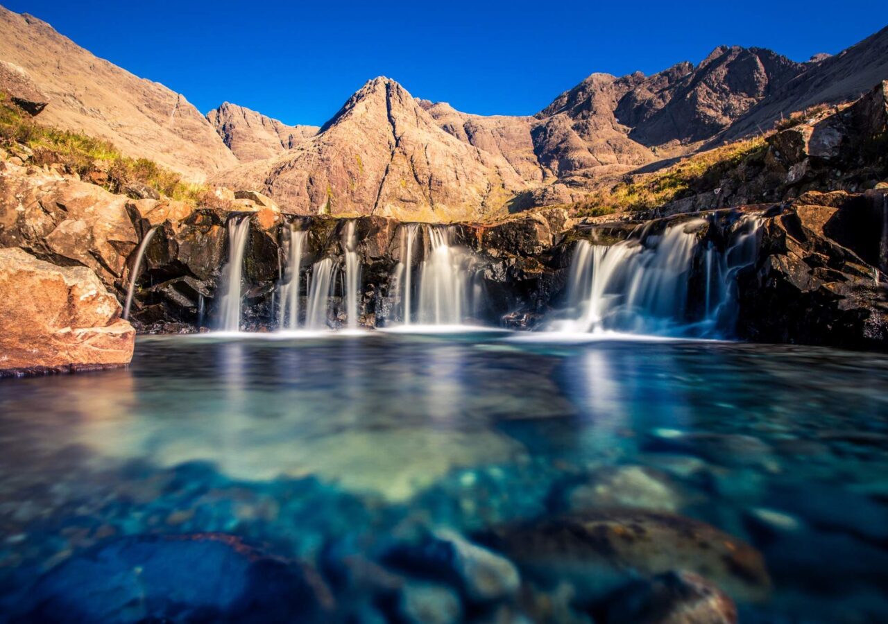 alt="Fairy Pools on the Isle of Skye with clear turquoise water and mountain backdrop"