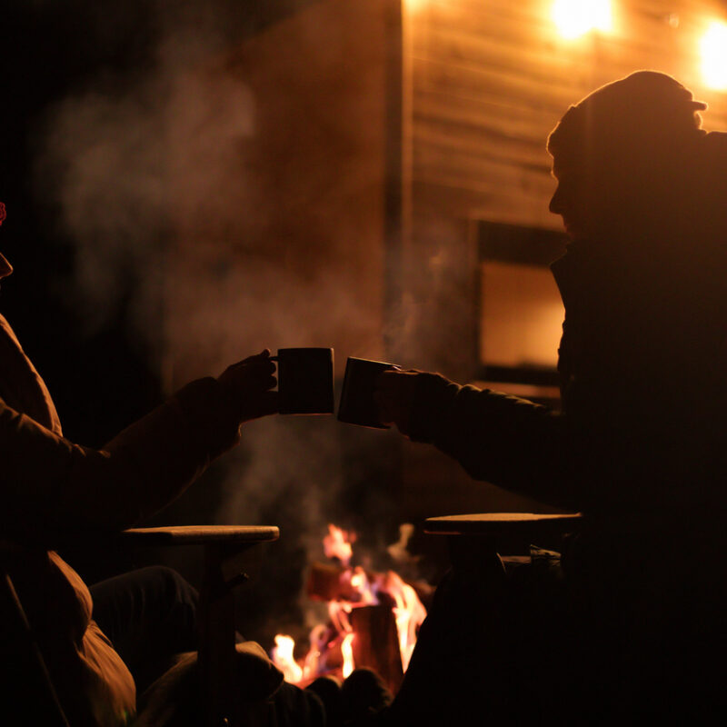 Two people sitting by a fire at night.