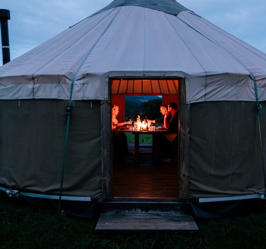 A lantern lit yurt at dusk with the fire burning inside