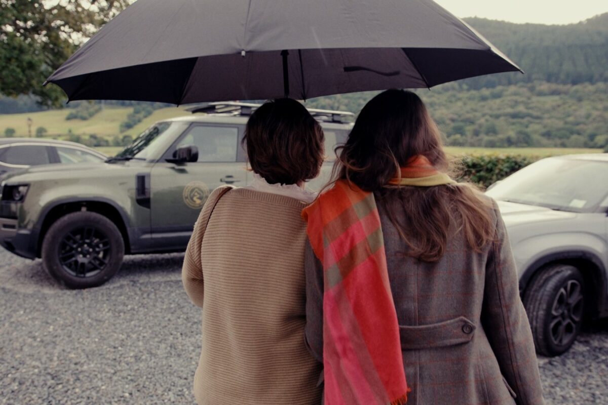 highland-reset-01-winter-drive Two people sheltering under an umbrella beside a Land Rover Defender