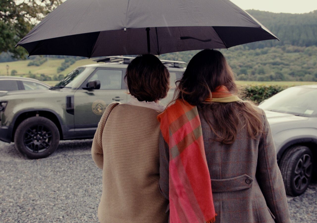 Two people sheltering under an umbrella beside a Land Rover Defender