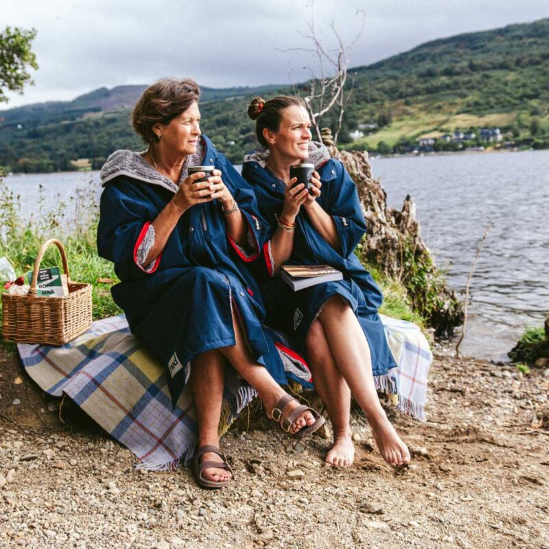Two people sitting beside a Highland loch with a drink