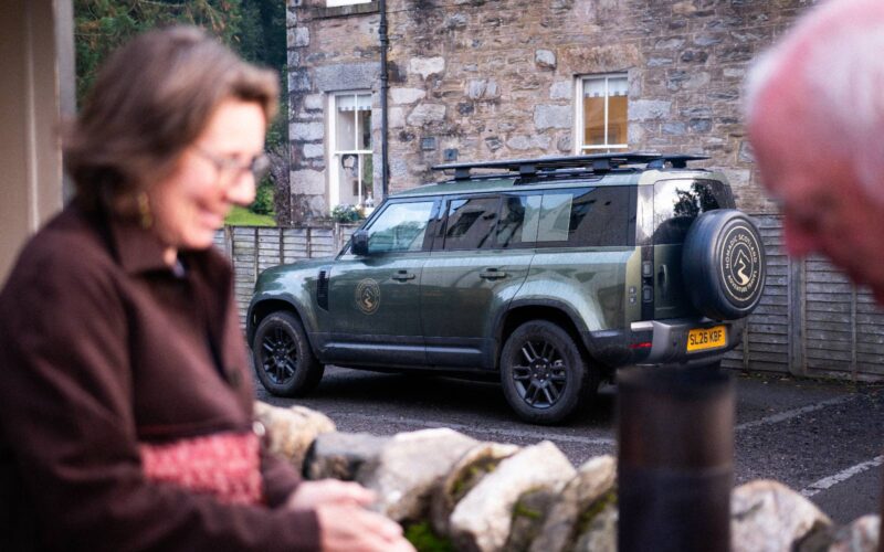 A guest beside a Land Rover Defender on a village street
